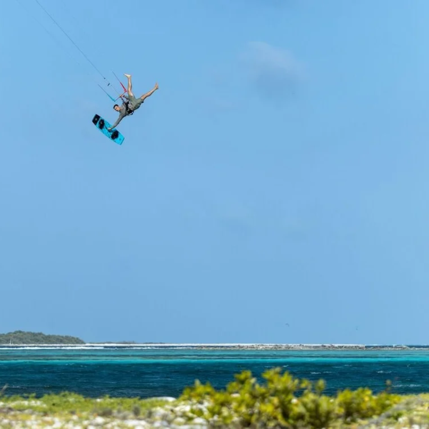 duotone-big-air-handle-alt3 Kitesurfer performing a big air jump with a board off grab high above a turquoise lagoon, riding the Duotone TS Big Air board with the Big Air Handle fitted.